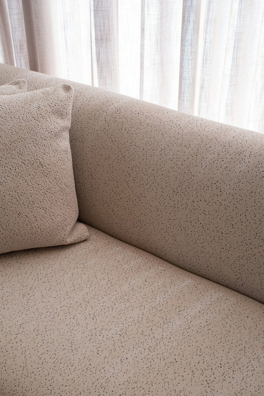 Sofá tapizado en tela texturizada color beige con cojín y cortinas